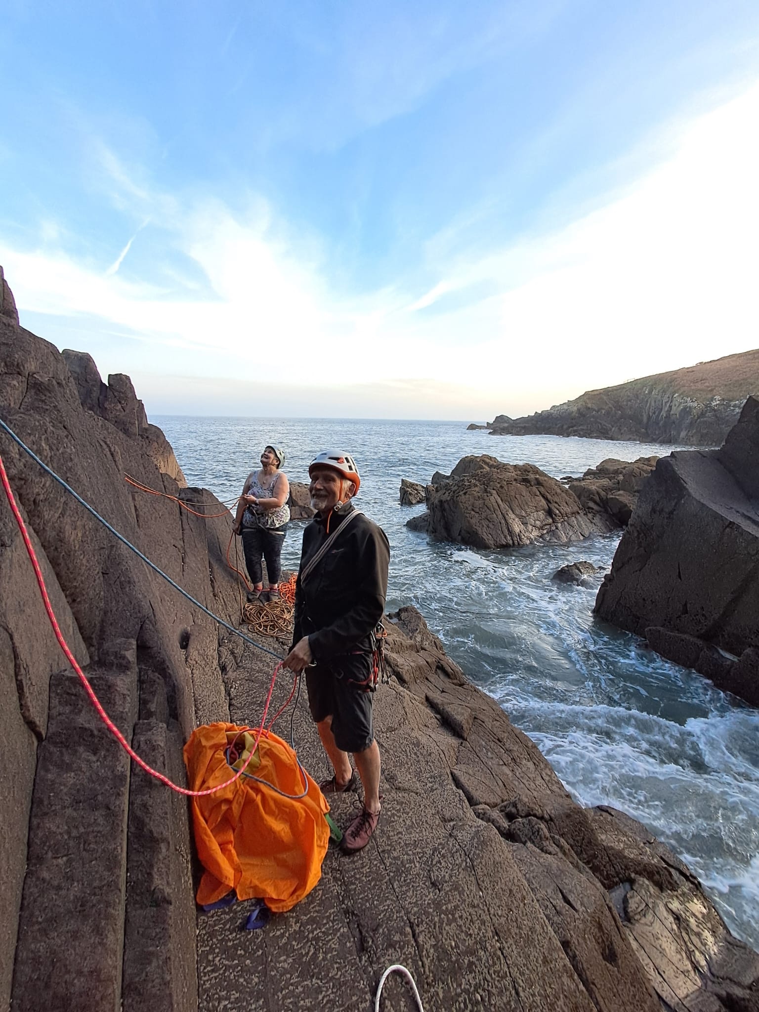 Two club members on the rocks above the sea at Porthclais, one holding the ropes running down the slab while the other coils a rope behind.